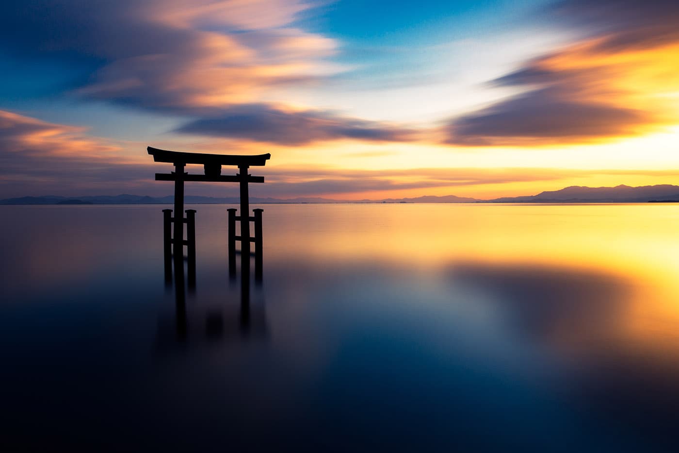 A torii gate standing in Lake Biwa under a glowing sunset sky.