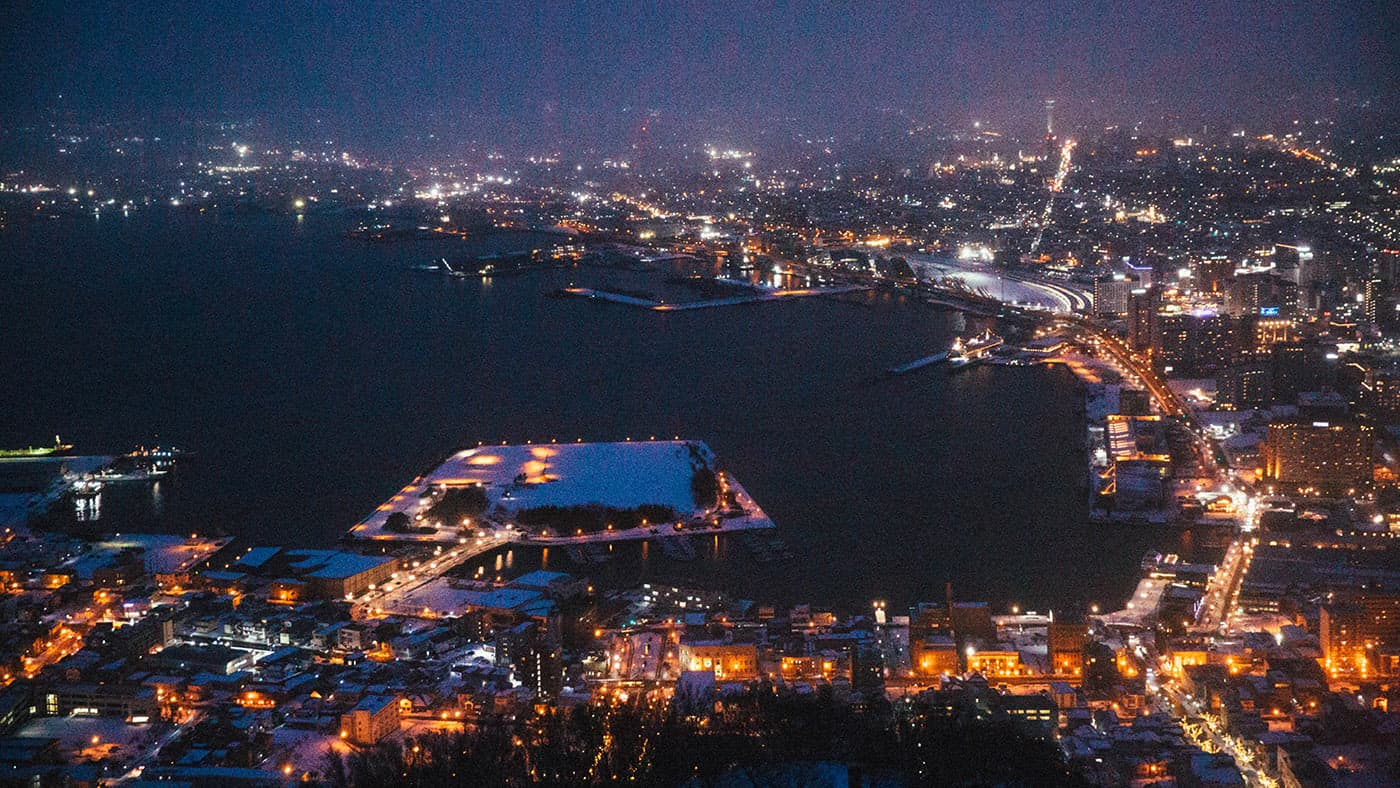 A blue-toned waterfront night view with mountains in the distance.