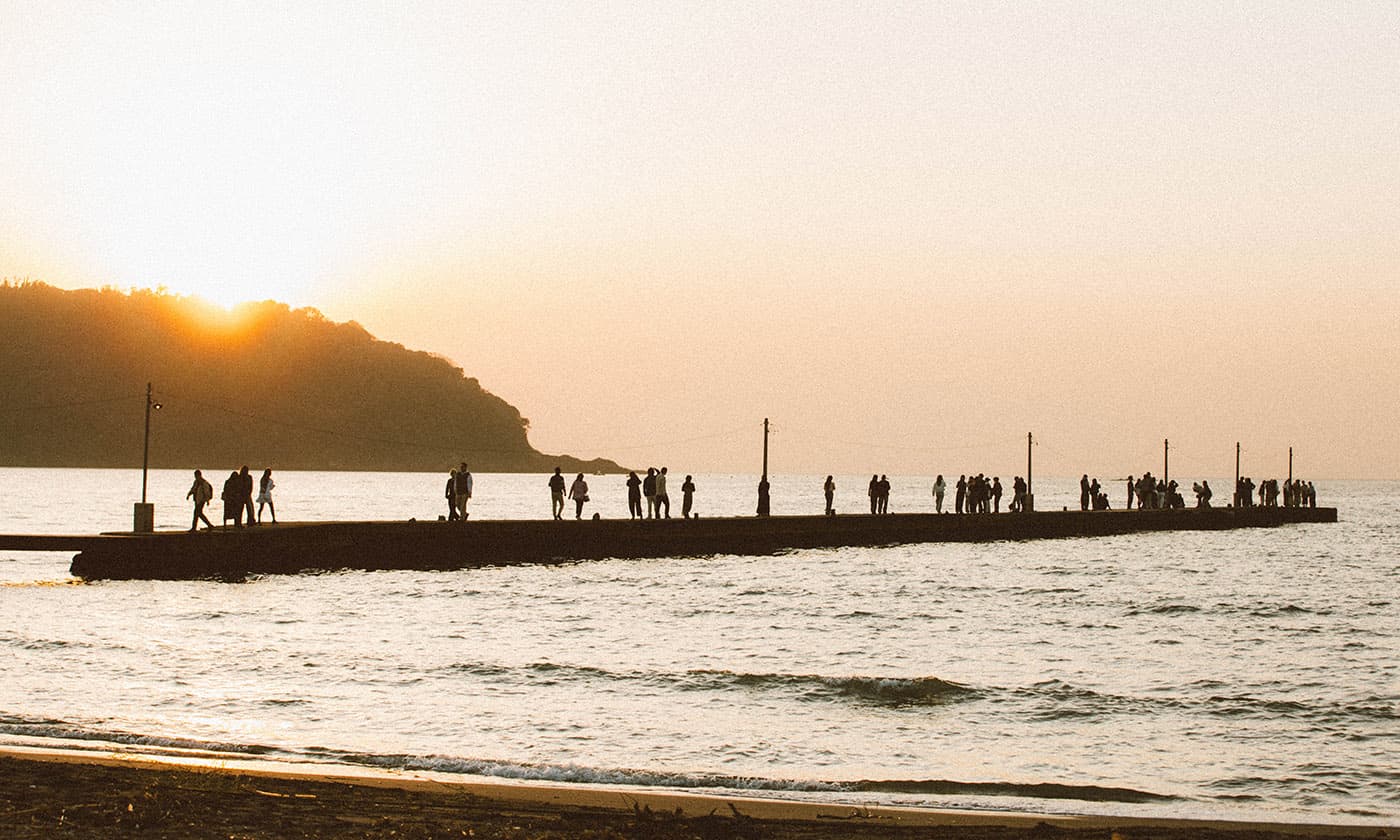 A wooden pier at sunset with small silhouettes at the far end.